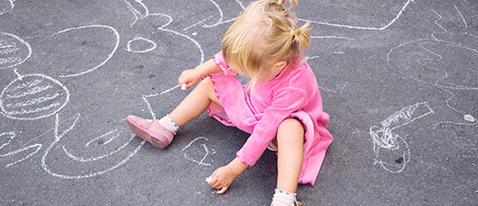 Foto: P. de Grenet Niña sentada en el suelo y haciendo dibujos con una tiza en el pavimento